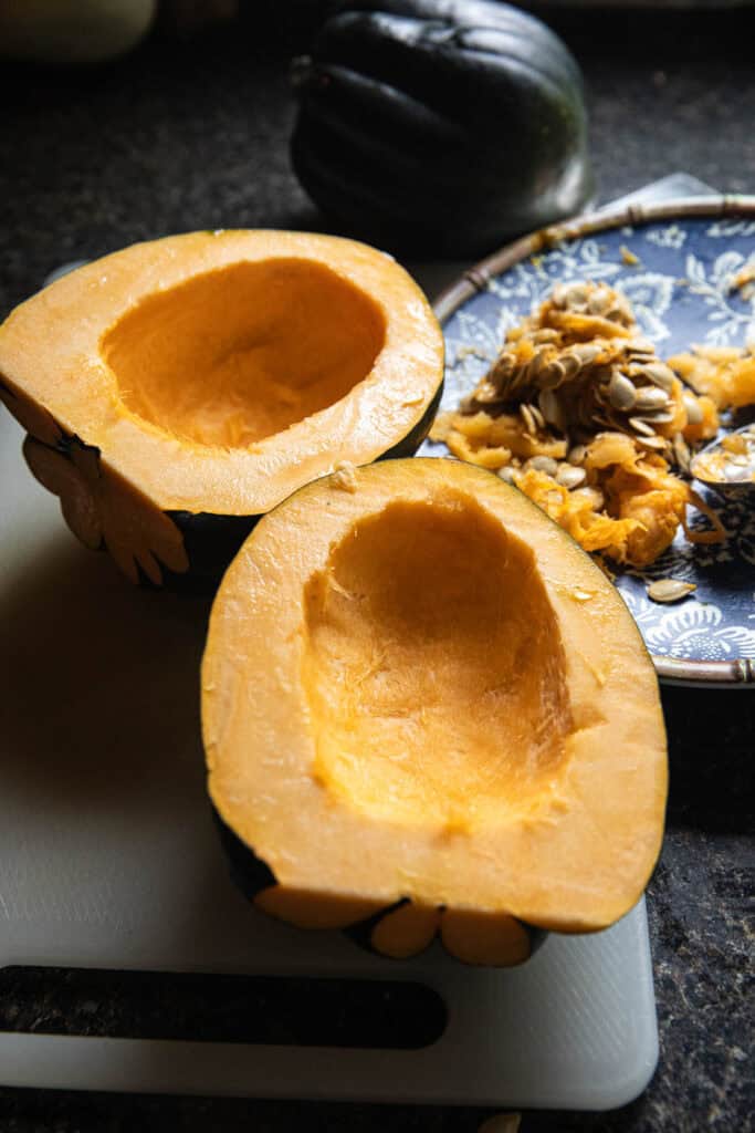 Halved acorn squash with seeds scooped out on a cutting board. 