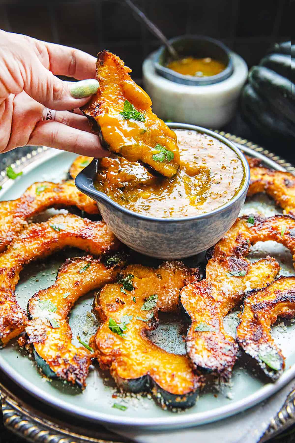 Roasted Acorn squash slices on a plate with a hand dipping a piece in a mango curry sauce.