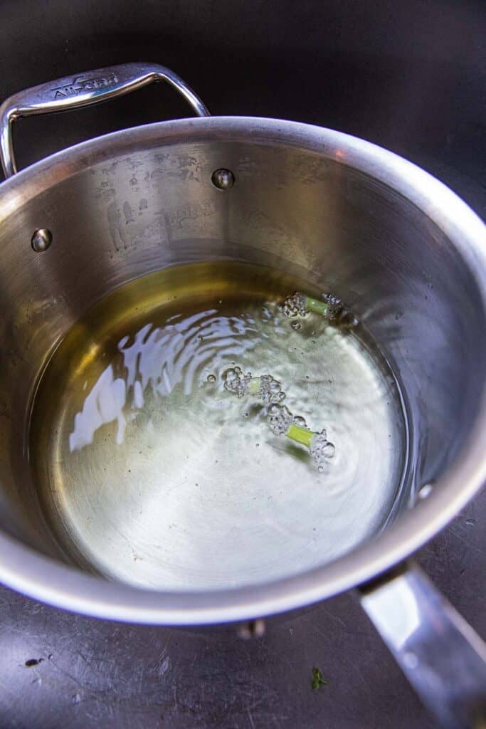 A pot of oil over the stove top with a couple of pieces of green onion. 