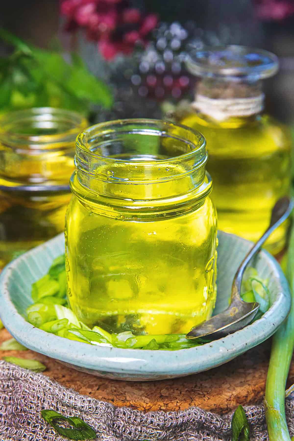 A glass bottle of mỡ hành or scallion oil on top of a small plate with chopped green onions on the bottom.
