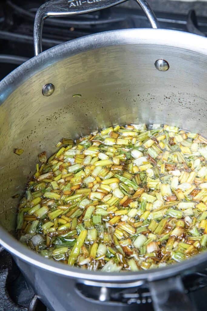 A pot frying fried green onions chunks in oil over a stove top.
