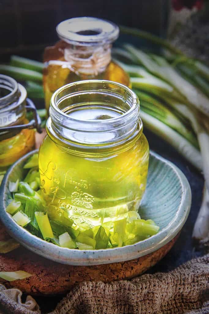 A glass bottle of mỡ hành on top of a small plate with chopped green onions on the bottom.