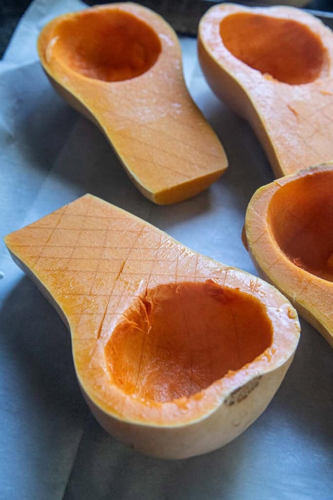 Four scored and Halves of kabocha squash on a baking tray. 