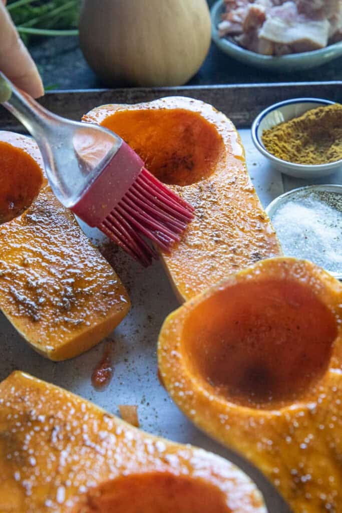 Four scored halves of kabocha squash, spiced with oil and seasoning, on a baking tray. 