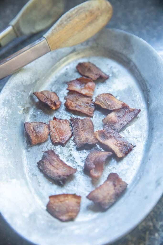 baked bacon pieces on a plate next to a tong. 