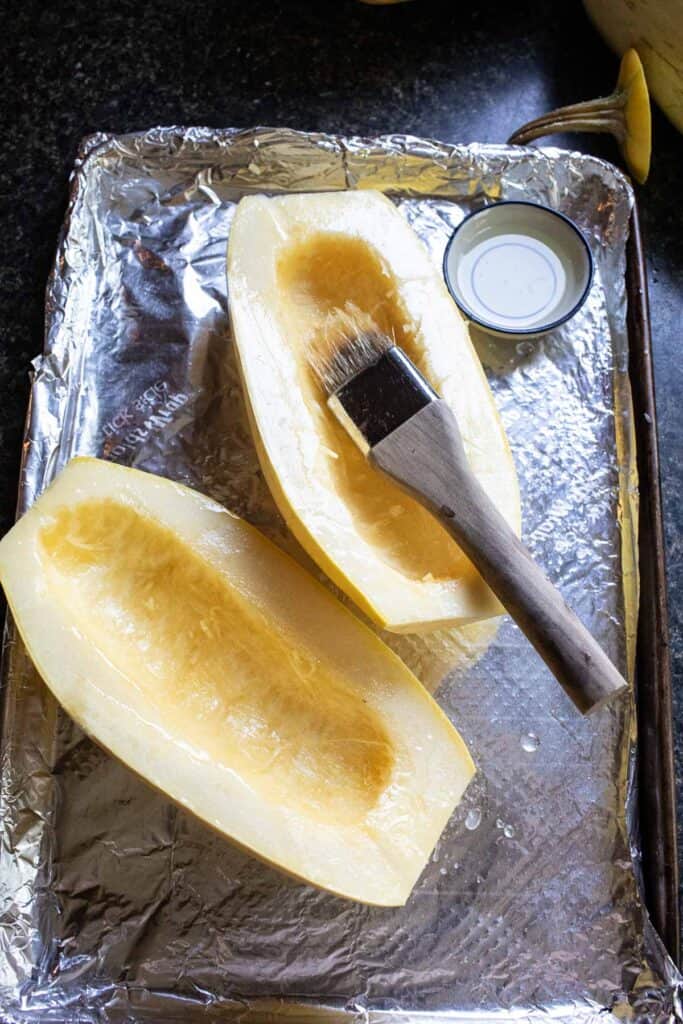 2 halves of spaghetti squash on a tray with a brush with oil on them. 