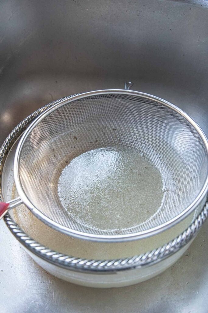 Fine mesh strainer on top of a bowl of pork broth. 