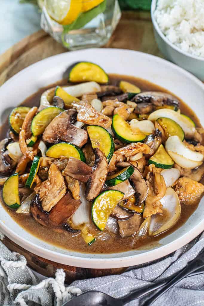 Chicken mushroom stir fry recipe on a platter on a cutting board with a spoon in the middle. 