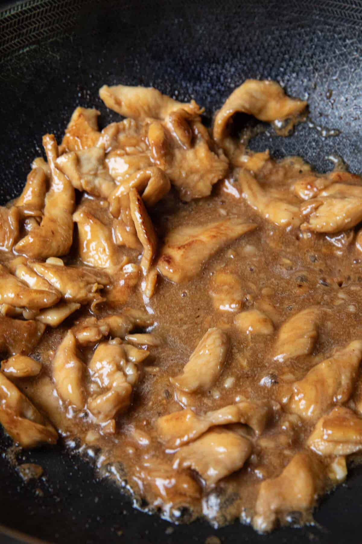 Sautéed brown chicken pieces in cornstarch slurry sauce in a wok. 