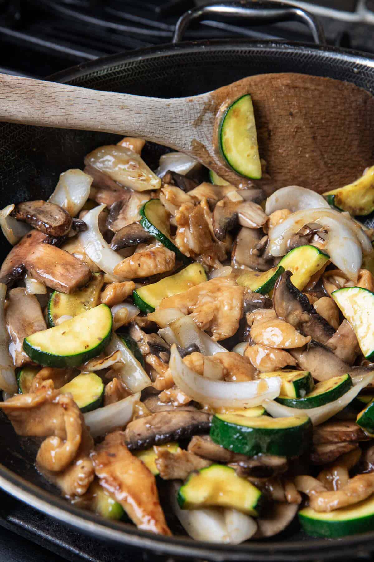 Sautéed chicken pieces, mushrooms, onion, and zucchini in a cornstarch slurry sauce in a wok. 