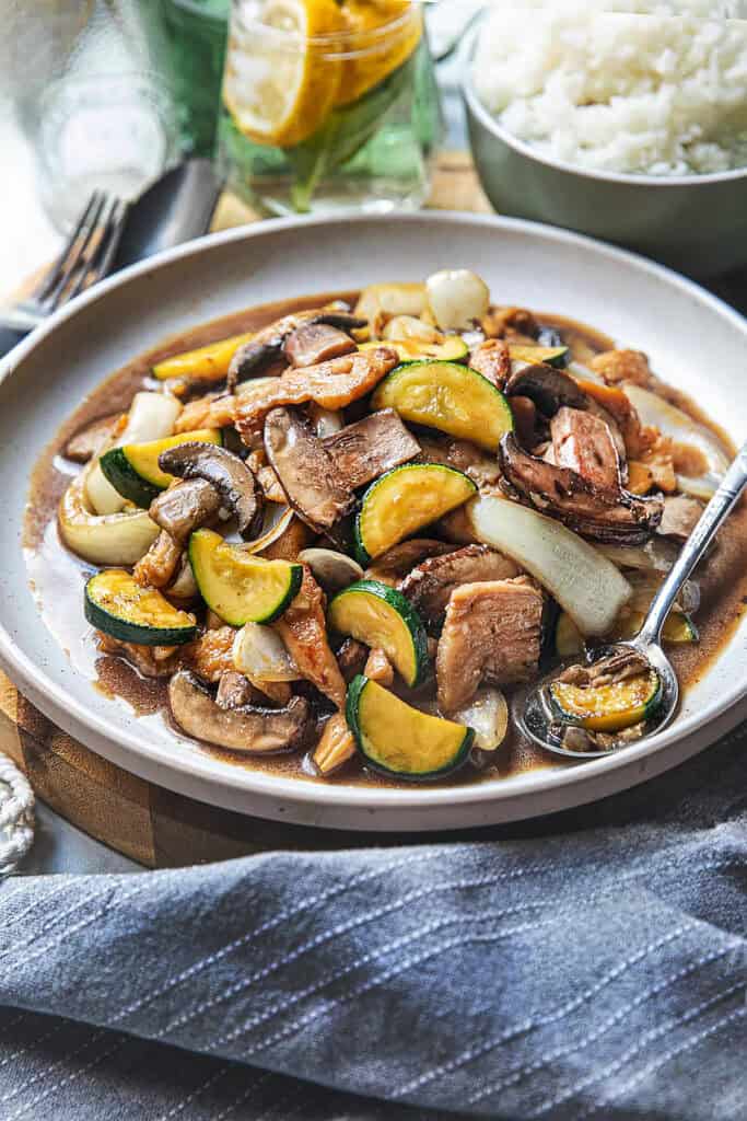 Chicken mushroom stir fry on a platter on a cutting board with a spoon in the middle. 