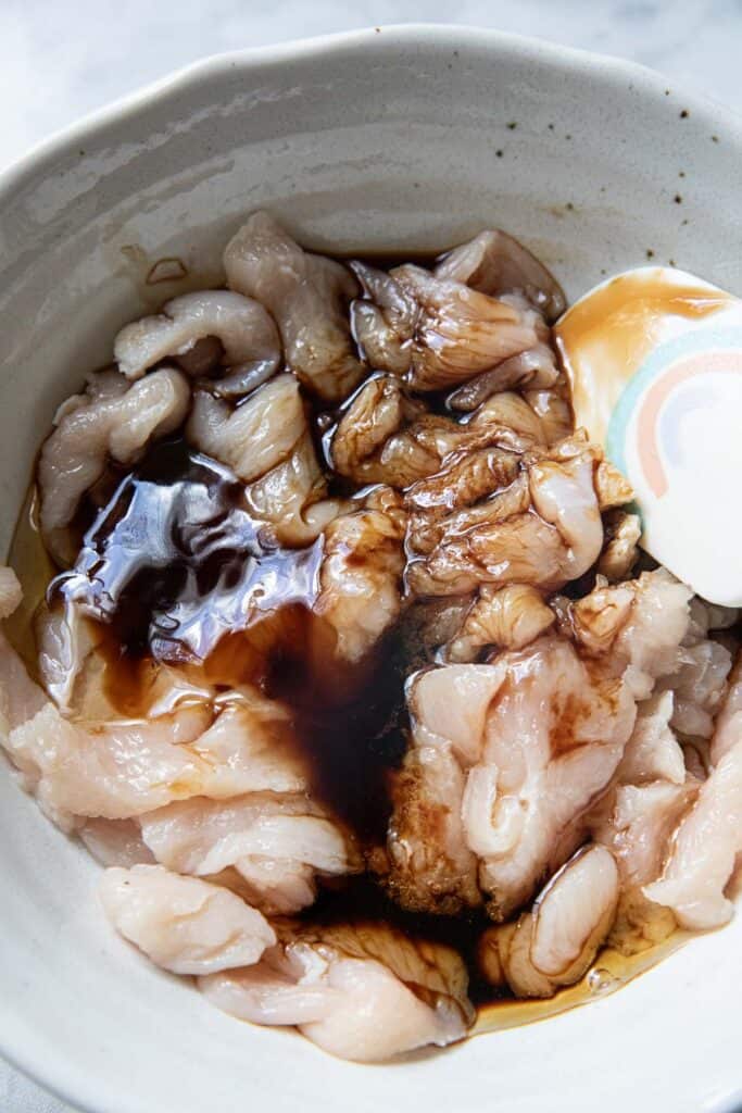 Chicken slices in a bowl with brown sauce mixed in. 