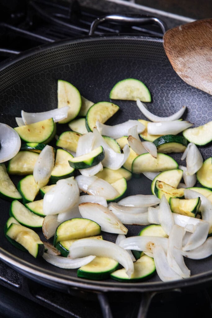 Sautéed sliced onion and zucchini in a pan. 