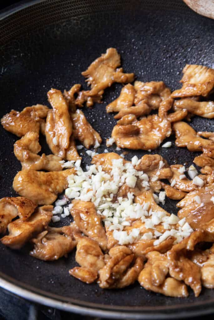 Sautéed brown chicken pieces and minced garlic in a wok. 