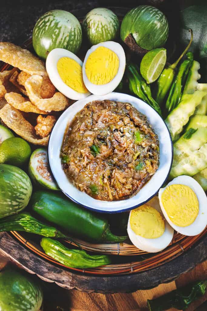 Nam Prik noom dip in a bowl surrounded by boiled eggs, veggies, and pork crackling.