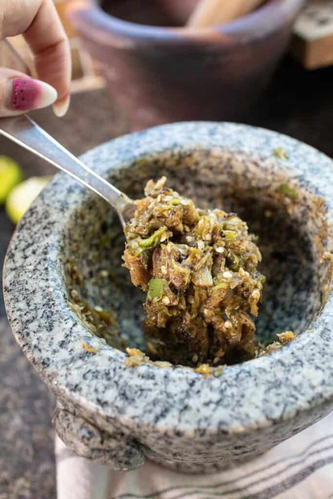 Hand holding a spoonful of nam prik noom from a mortar.