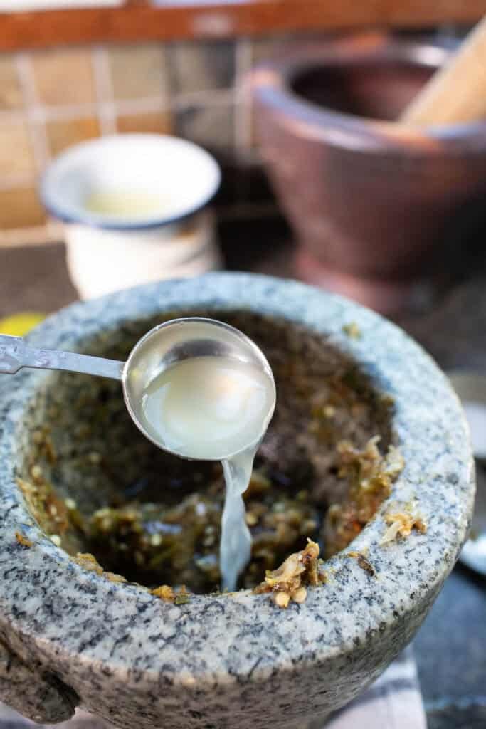 Nam Prik Noom dip in a stone pestle with lime juice pouring into it.