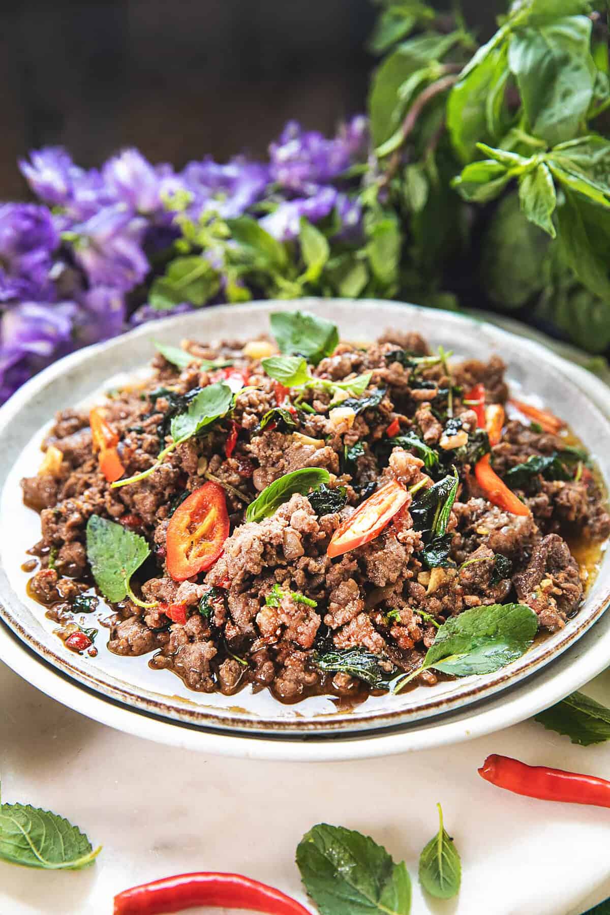 Thai beef basil stir fry on a plate with holy basil leaves on the sides. 
