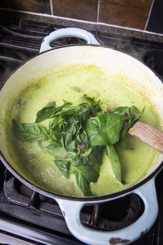 basil leaves onto of a pot of green soup on the stove. 