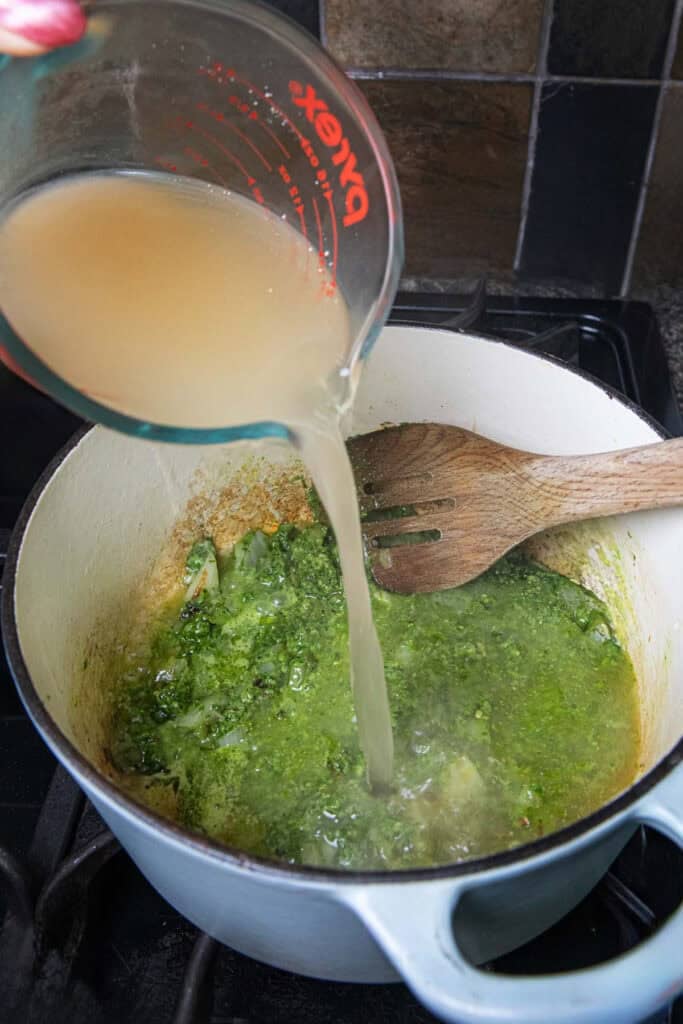 Stock pouring into a pot of green soup on the stove. 