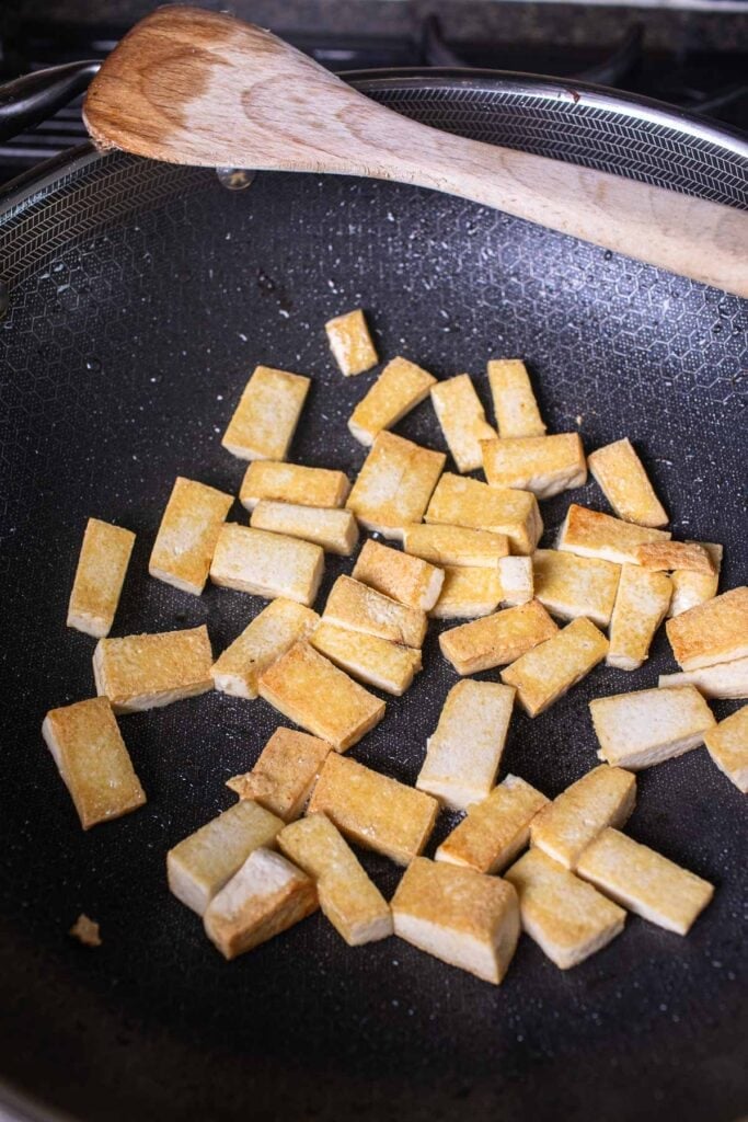 Fried cubed firm tofu in oil in a wok.