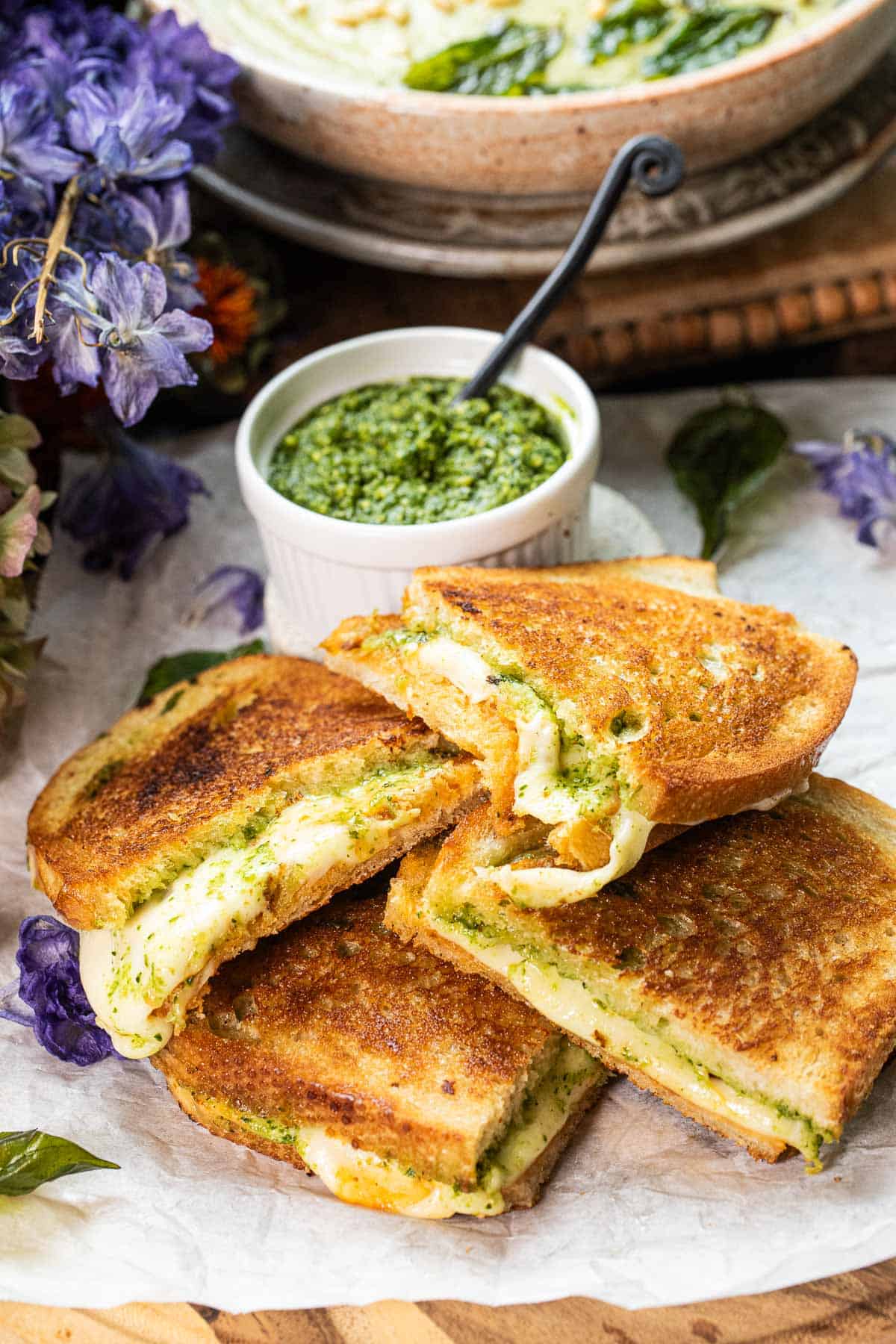 4 pieces of Thai basil pesto grilled cheese stacked on top of each other on a baking sheet with a small bowl of pesto sauce.
