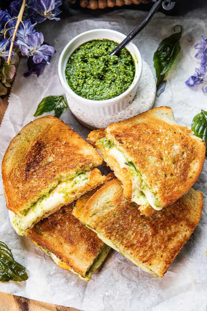 4 halves of Thai basil pesto grilled cheese stacked on top of each other on a baking sheet with a small bowl of pesto sauce.