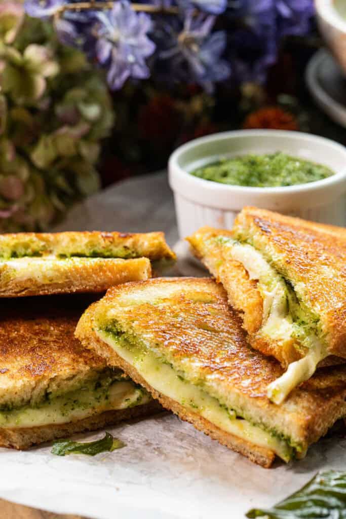 Sliced pesto cheese sandwiches are stacked on top of each other on a baking sheet.