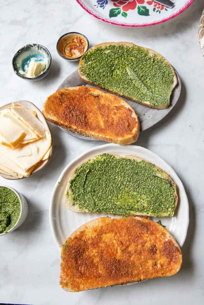 Slices of bread spread with pesto sauce and tom yum paste on top of a table.
