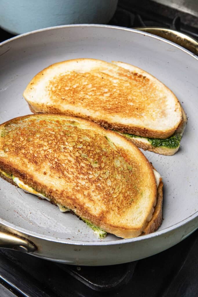 Two Tom Yum pesto sandwiches are frying in a pan.