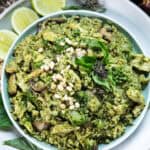 Pesto rice in a plate on the table with lime wedges as garnish.