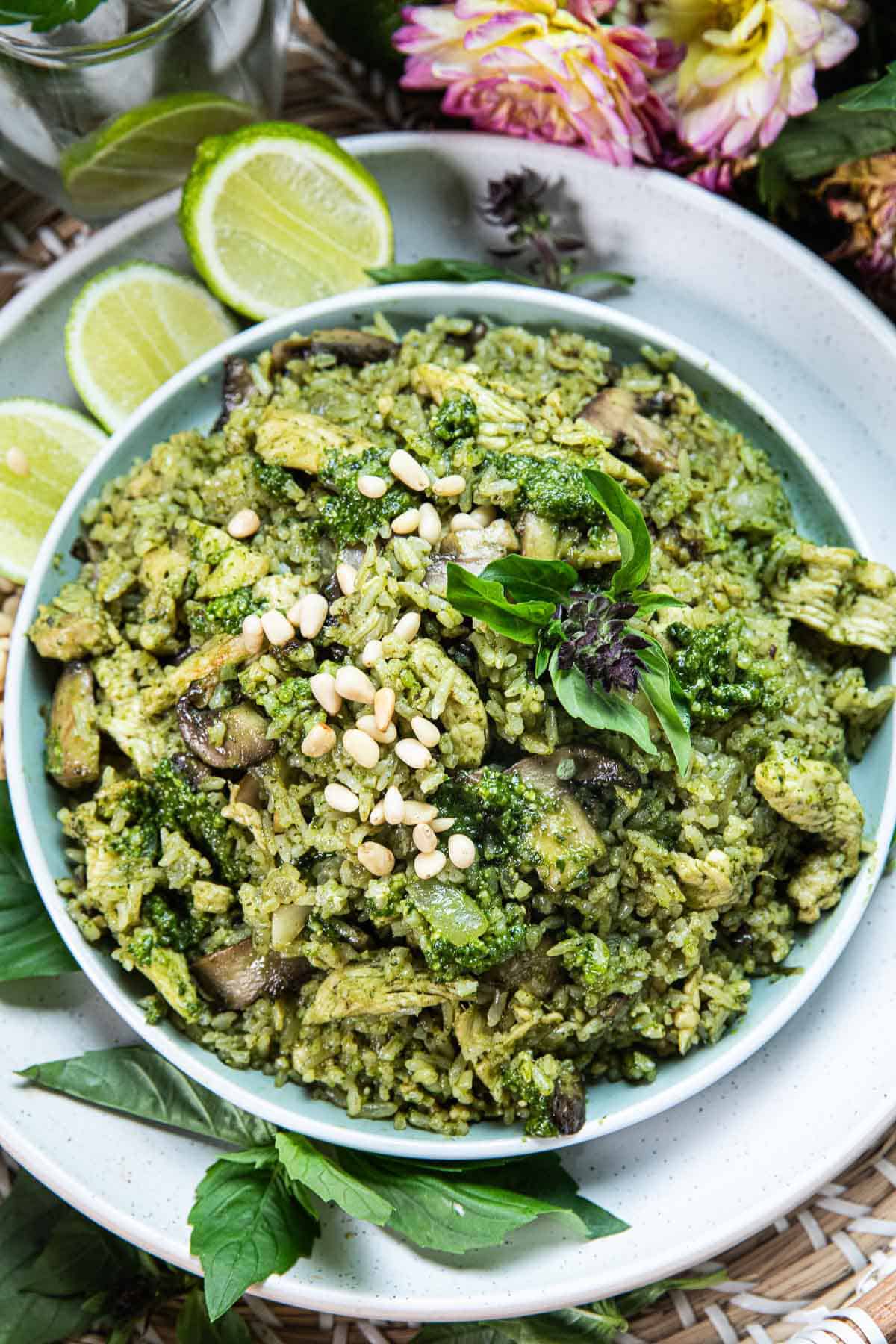 Thai basil pesto rice in a platee wedges, with basil, lim and flowers around as garnishes on a table.
