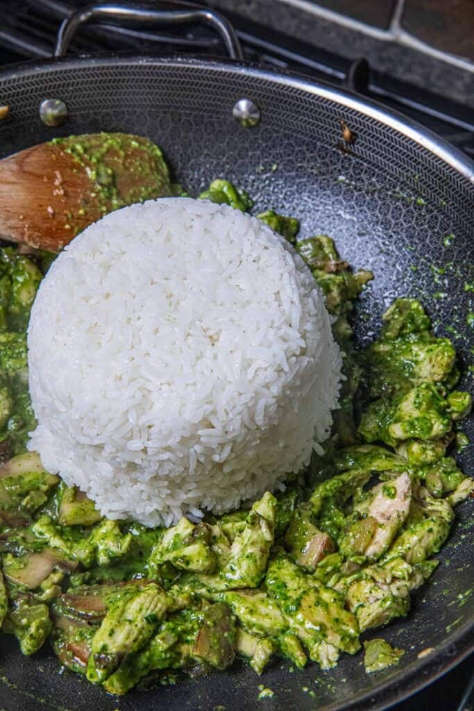 A scoop of jasmine rice on top of green chicken pesto stir-fried in a wok.