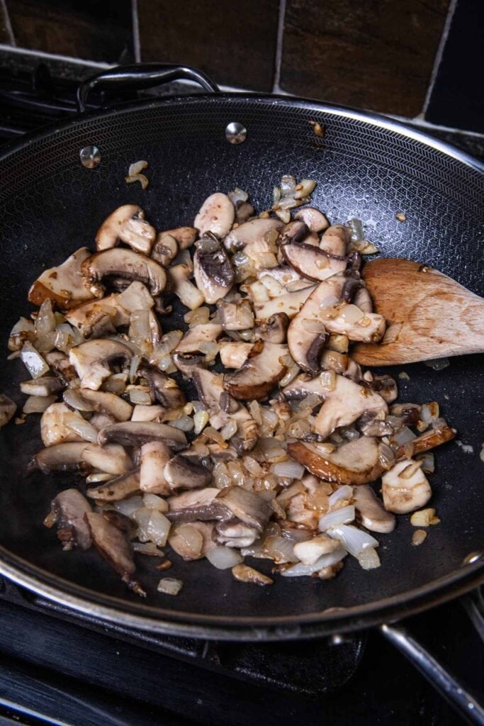 Sautéed onion, garlic, and mushrooms in a wok.