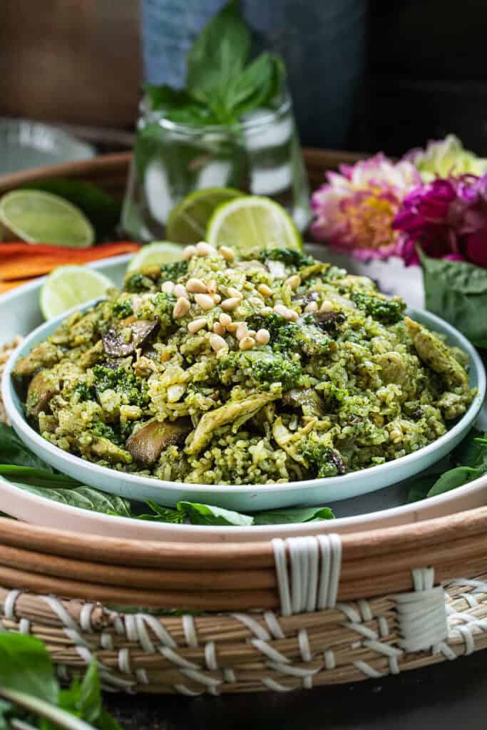 A plate of Thai basil pesto fried rice with lime wedges and flower garnishes sitting on top of a table.