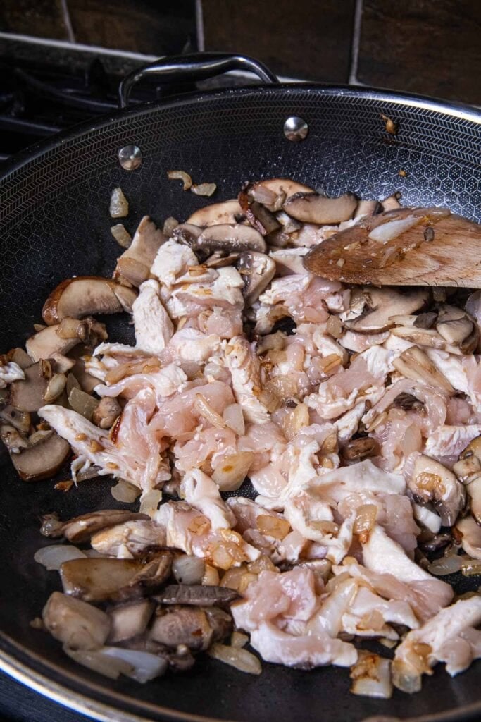 Sautéed onion, garlic, chicken, and mushrooms in a wok.