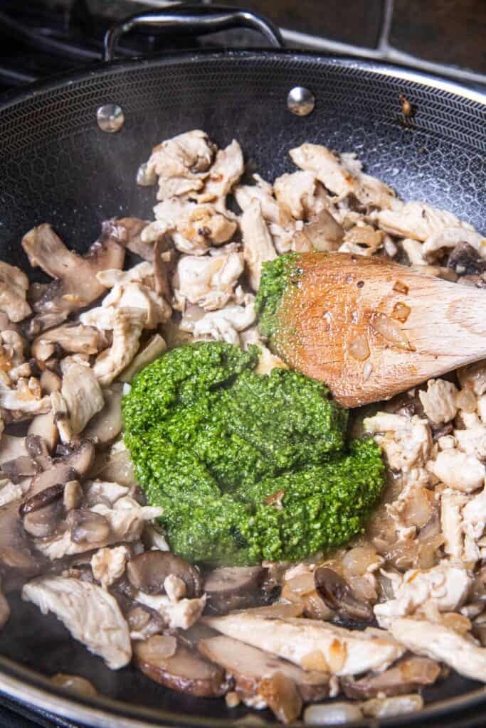 A pile of Thai basil pesto sauce on top of, mushrooms, and onions sauteed chicken in a wok.