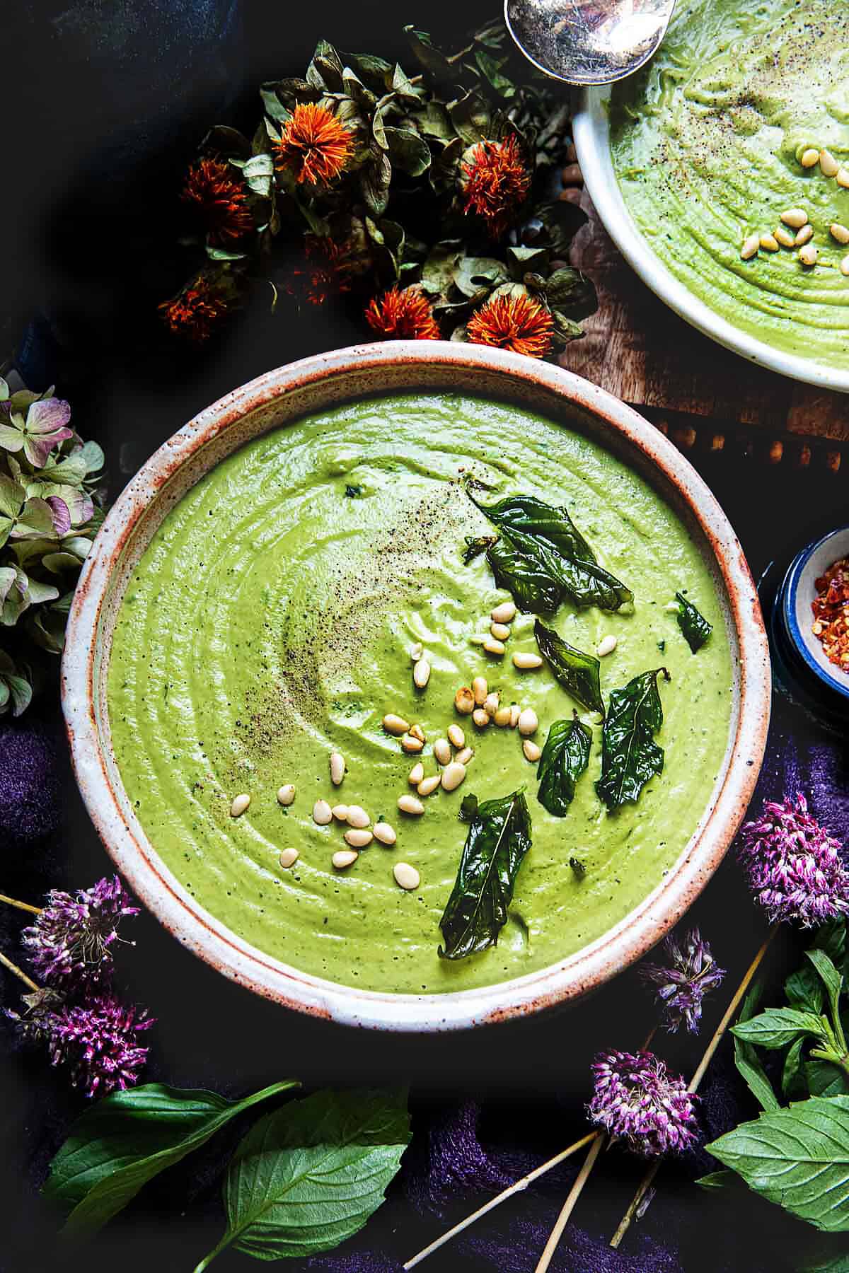 Creamy pesto soup in a bowl with pine nuts and fried Thai basil leaves garnishes on top. 