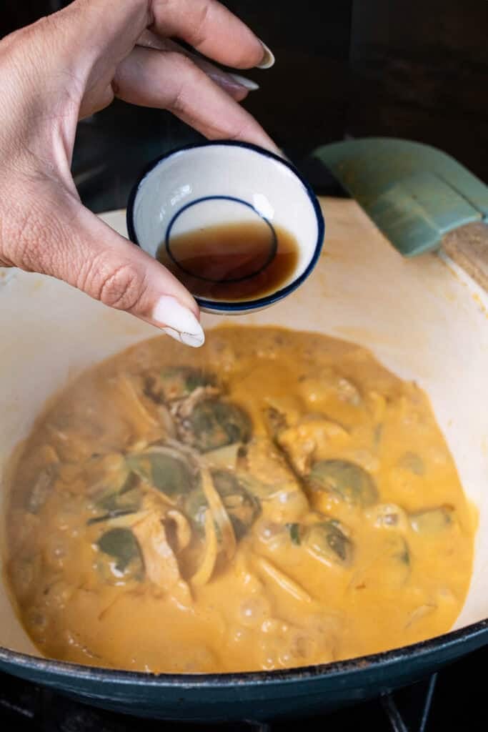 Hand holding fish sauce in a small bowl over Thai eggplant curry.
