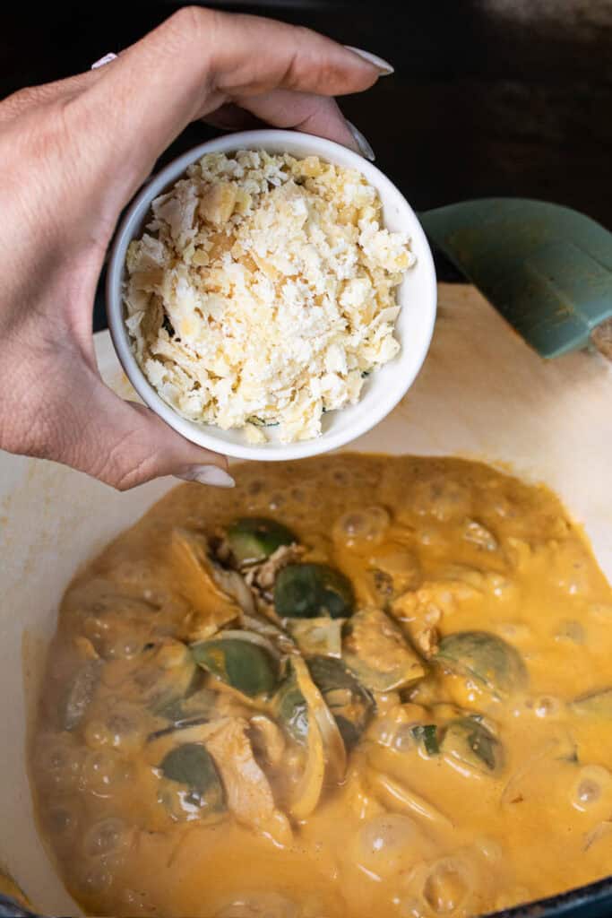 Hand holding palm sugar in a small bowl over Thai eggplant curry.