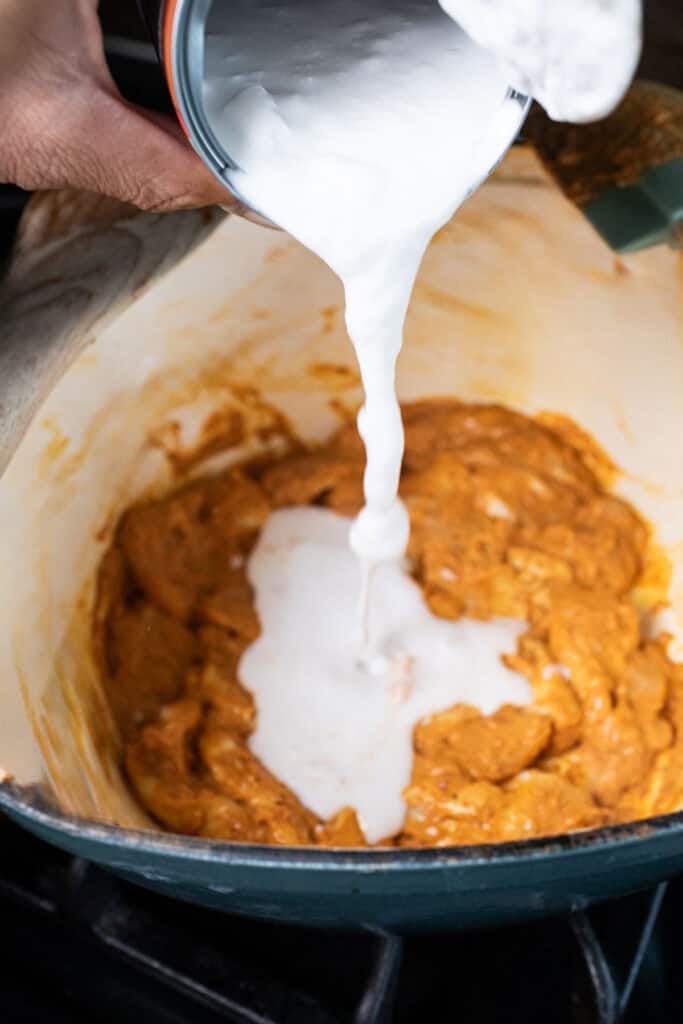 Coconut milk pouring into a pot of red curry sauce.