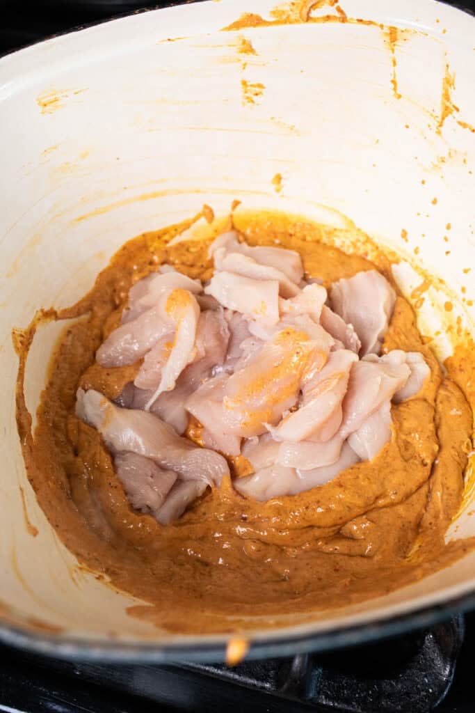 Chicken slices in a pot of red curry sauce.