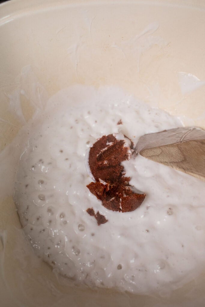 Coconut milk in a pot with a spoonful of red curry on top.