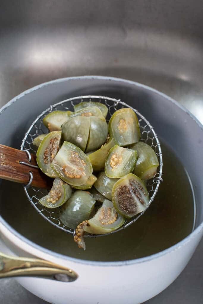 Strainer lifting boiled sliced Thai eggplant over a pot of water. 