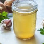 Thai vegetable stock in a glass jar on the table with herbs around it.