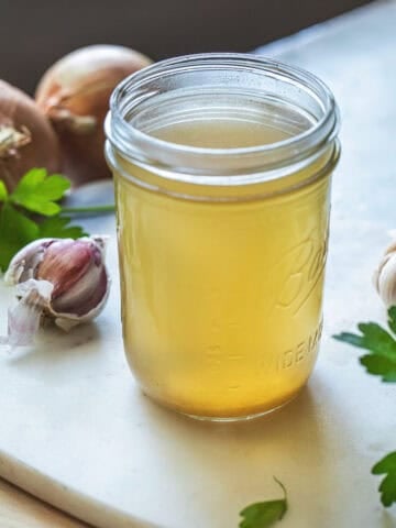 Thai vegetable stock in a glass jar on the table with herbs around it.
