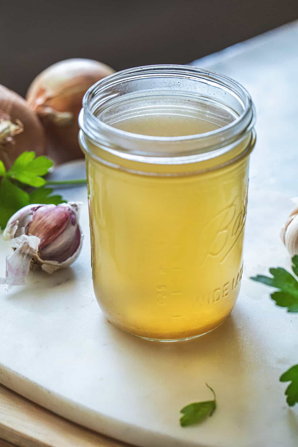 Thai Vegetable Stock in a glass jar, on a table surrounded by herbs.