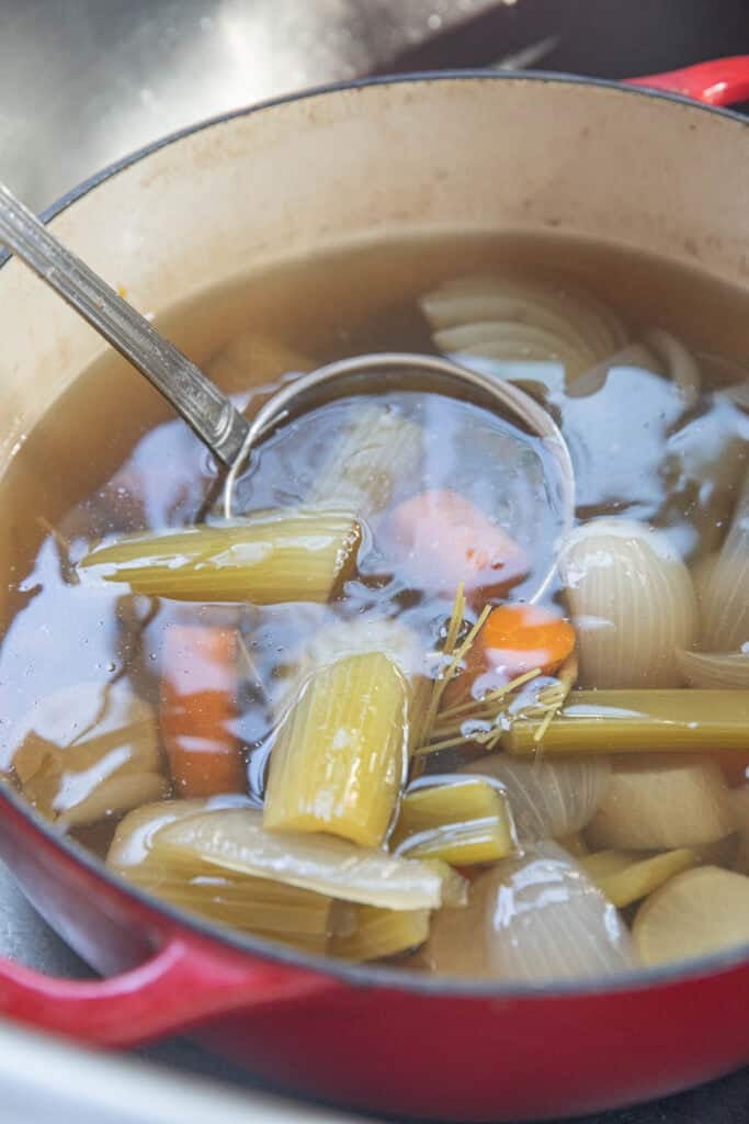 A ladle in a pot of vegetable stock with all the cooked veggies and broth.