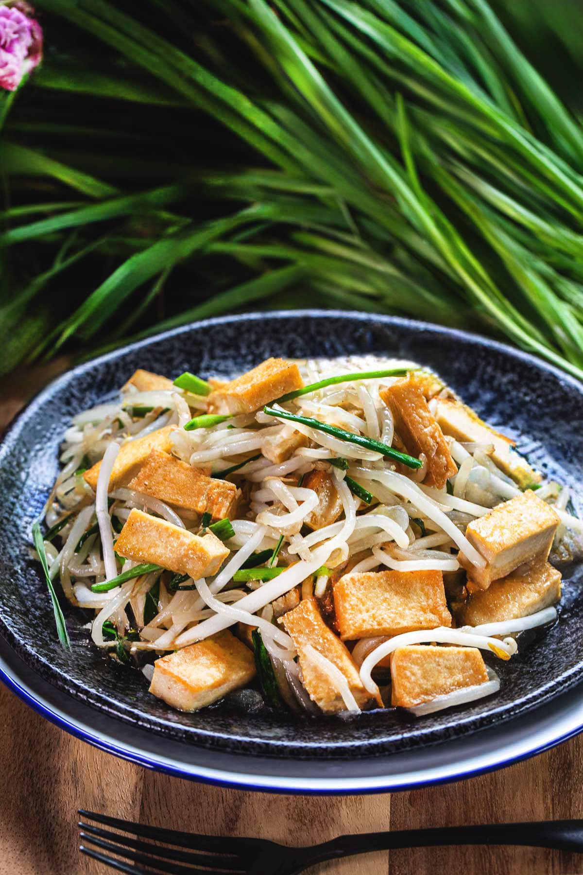 stir fried bean sprouts with chives and tofu in a plate with green chives on the side. 