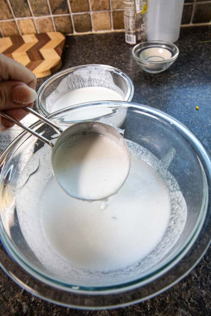 A measuring cup inside coconut mixture for thai coconut pancakes.